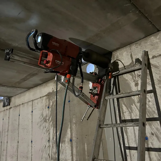 Kjerneboringsutstyr montert på en betongvegg under et tak med en stige ved siden av.