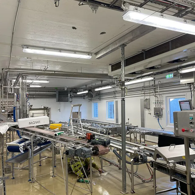 Industrihall med transportbånd og elektriske installasjoner under vedlikeholdsarbeid.