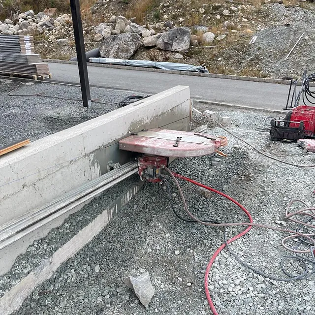 Betongsag festet til en lav mur utendørs, med rødslanger på grusdekket bakke.